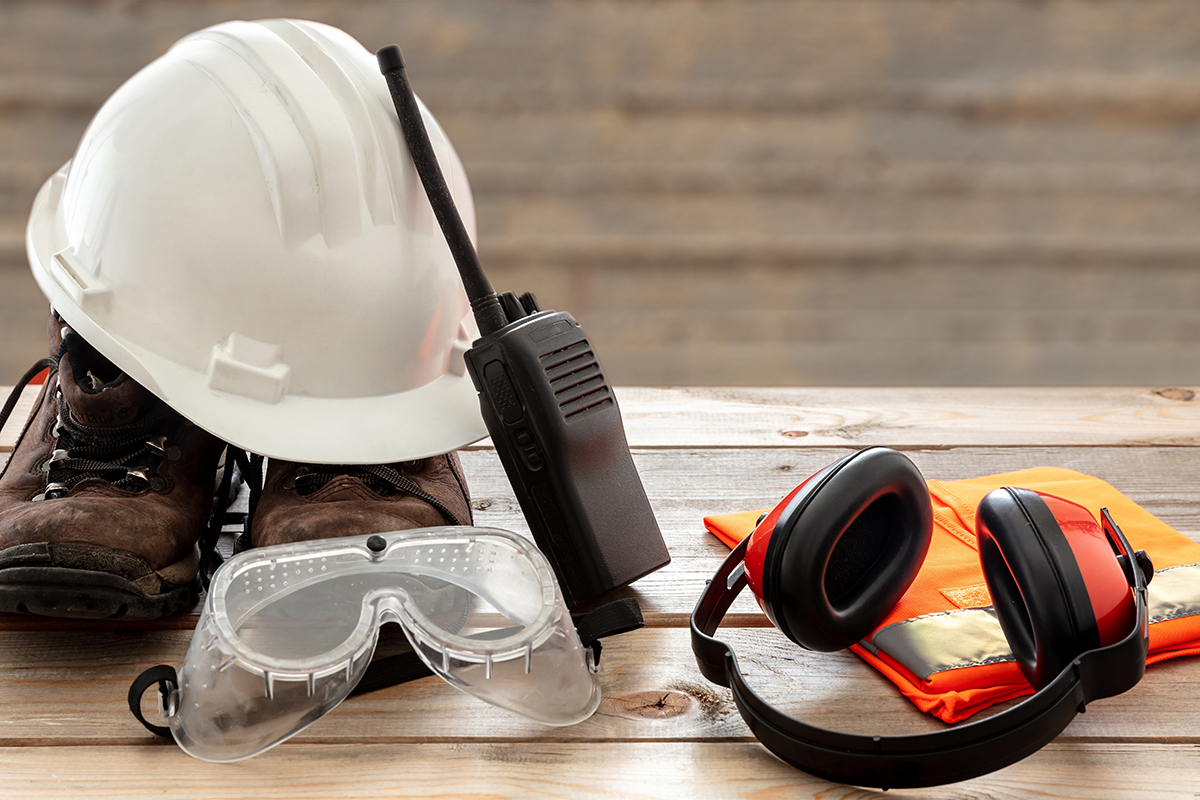 helm, veiligheidsschoenen, bril, walkie-talkie, oorbescherming en fluojasje op houten tafel, allemaal hulpmiddelen voor veiligheid op het werk